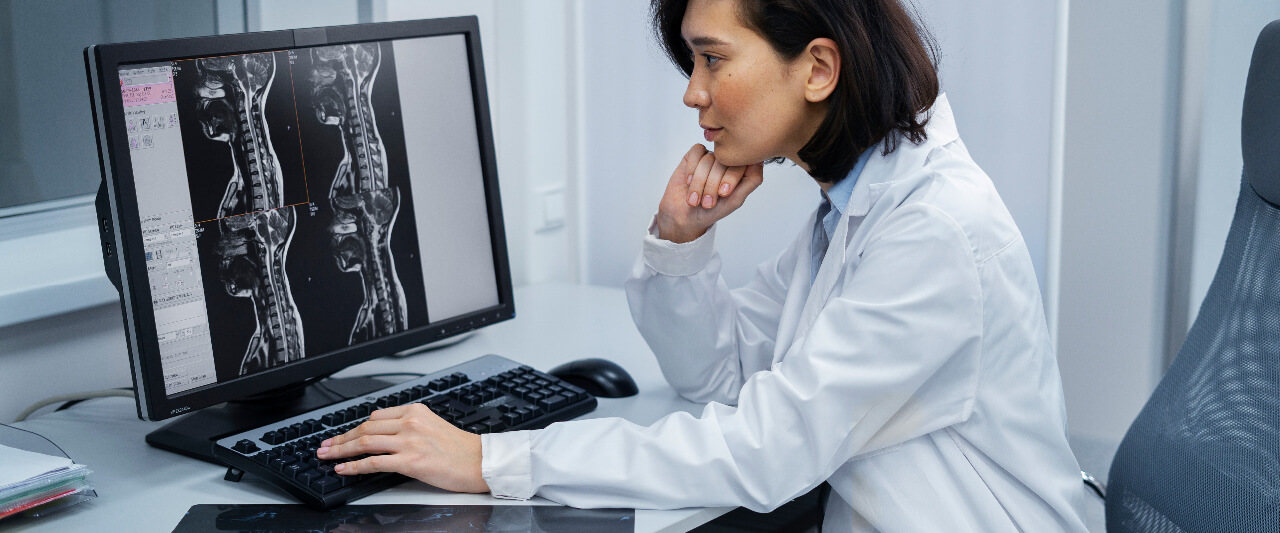 Radiologist sitting at workstation on computer reviewing scans.